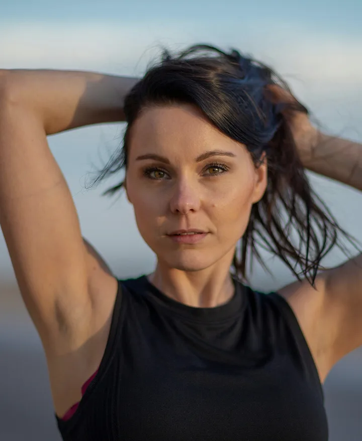 A woman outdoors at dusk, hands in her hair, looking into the camera